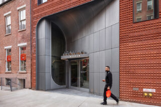 Exterior shot of the Italian Art Museum entrance point, a gray perforated metal facade. A person walks along the sidewalk.