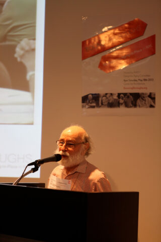 An older white man standing at the podium, speaking into a microphone.